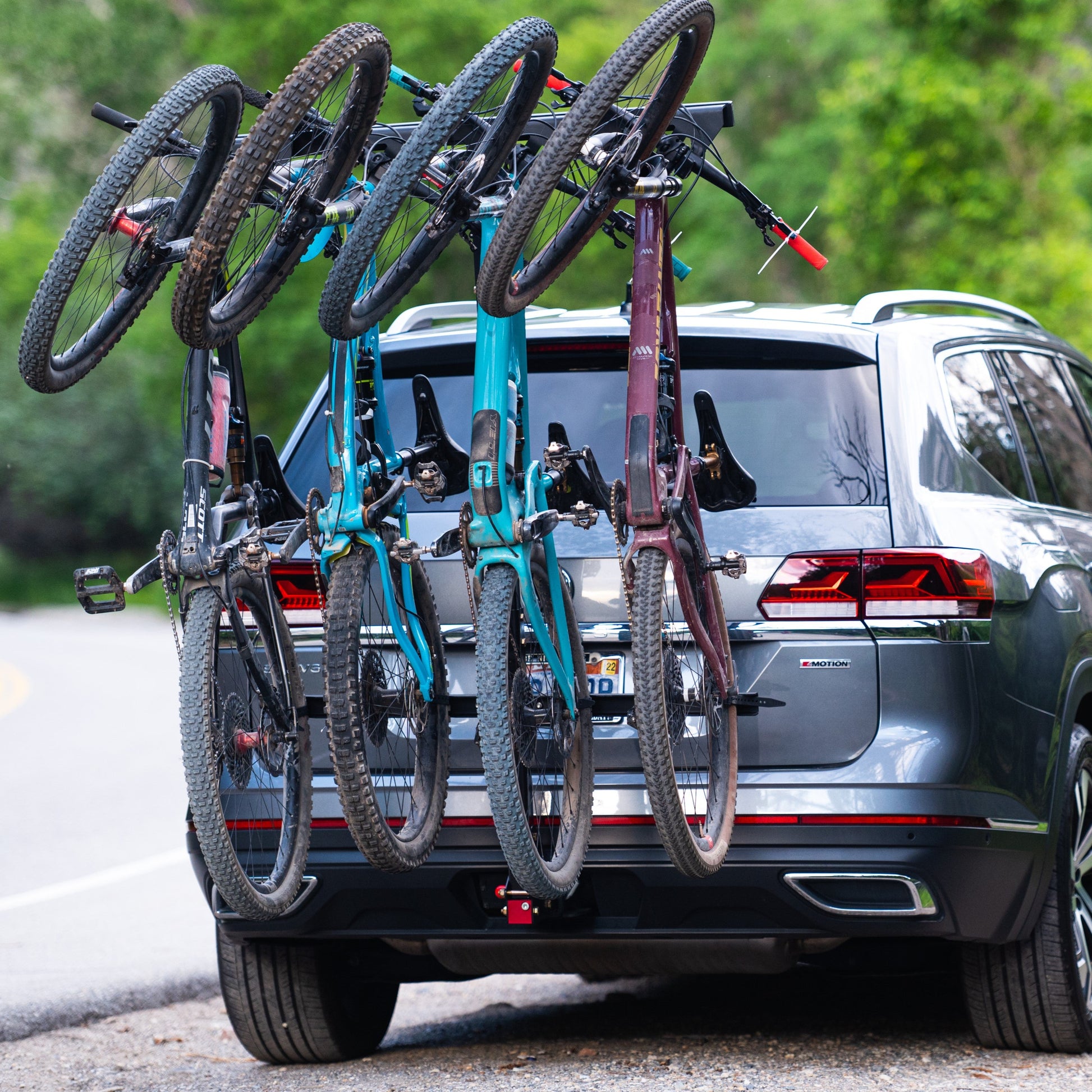 A vertical 4-bike rack mounted on the rear of a car, featuring adjustable handlebar hooks and carrying two bikes.