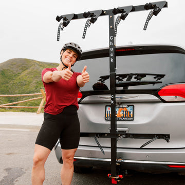 Person giving thumbs up next to a car with a bike rack on a mountain road.
