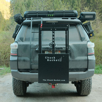 Back view of a vehicle with roof racks and 'Chuck Bucket' branding in a forest setting