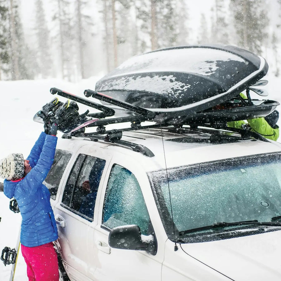 Person reaching up to load skis on a tall vehicle